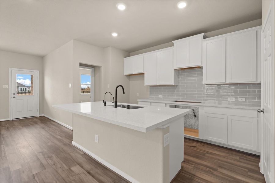 This light and bright kitchen features a large quartz island, white stained cabinets, a large sink over looking your family room, recessed lighting, and beautiful backsplash.