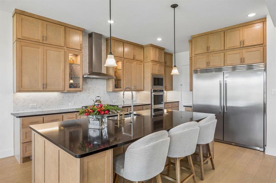 Kitchen with built in appliances, light wood finish cabinetry, a center island with sink, pendant lighting, and light wood-style flooring