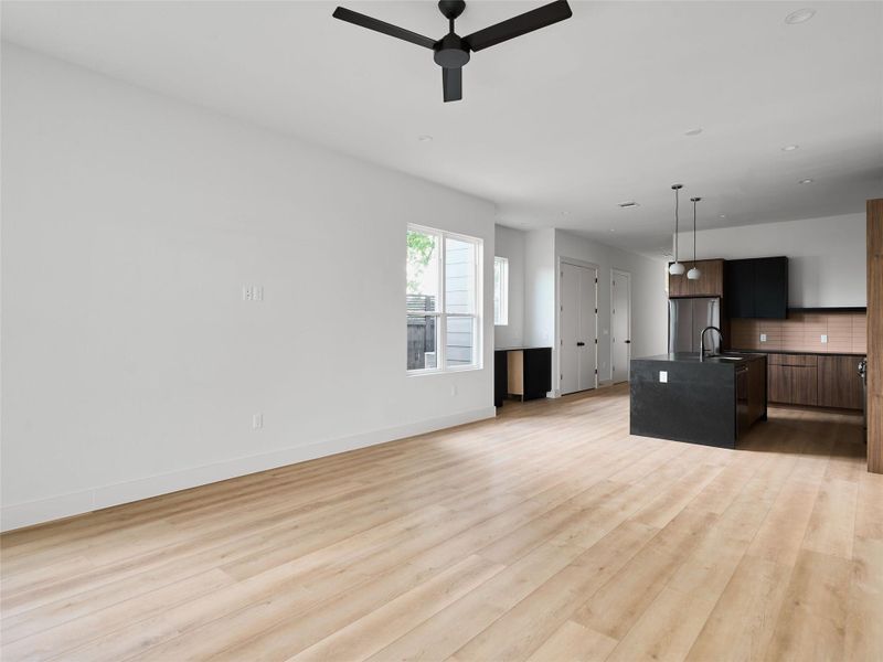 Kitchen featuring open floor plan, a center island with sink, decorative light fixtures, freestanding refrigerator, and light wood-style flooring Kitchen featuring open floor plan, a center island with sink, decorative light fixtures, freestanding refrigerator, and light wood-style flooring
