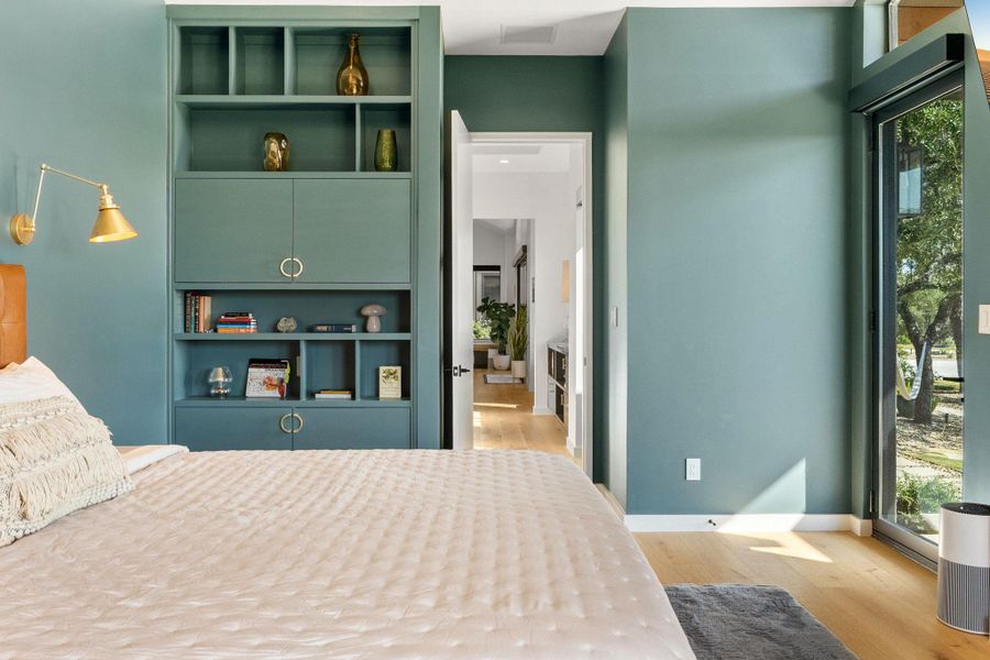 Built-in shelving unit with open display areas and closed cabinetry, a brass wall sconce, light wood-finish flooring, and a full-height glass door