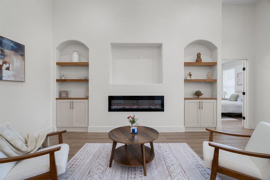 Living room featuring built in shelves, a glass covered fireplace, and light wood-style flooring Living room featuring built in shelves, a glass covered fireplace, and light wood-style flooring