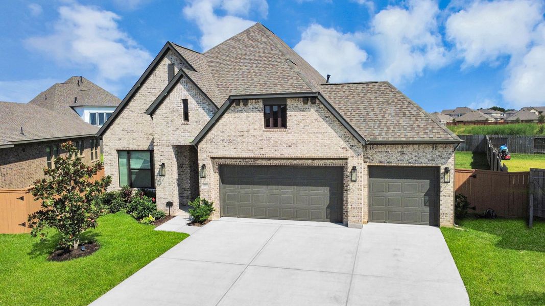 Charming brick home with a spacious three-car garage, lush green lawn, and inviting entrance, set in a tranquil neighborhood.