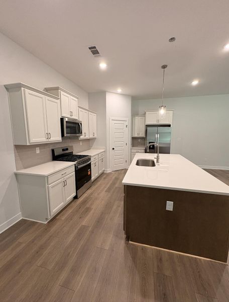 White cabinetry with crown molding, stainless steel appliances, wood-finish flooring, white countertops, and a central island with an integrated sink