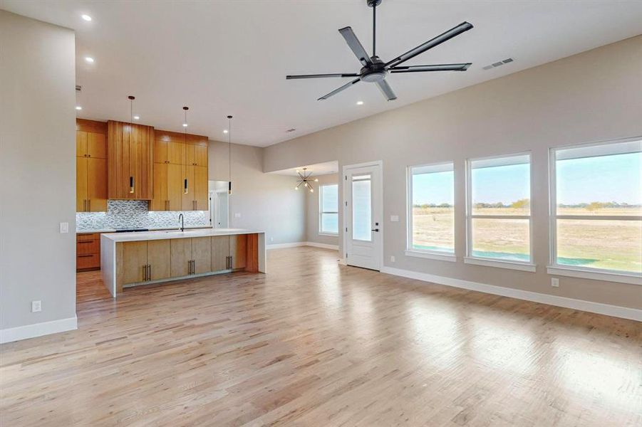 Kitchen featuring decorative backsplash, a spacious island, light wood-type flooring, pendant lighting, and sink