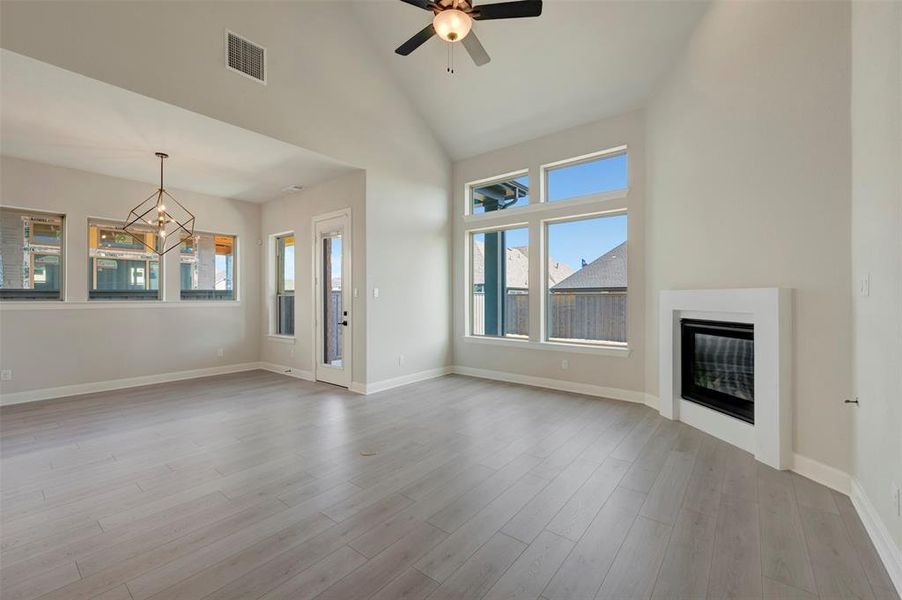 Unfurnished living room featuring vaulted ceiling, a glass covered fireplace, a ceiling fan, and light wood-type flooring