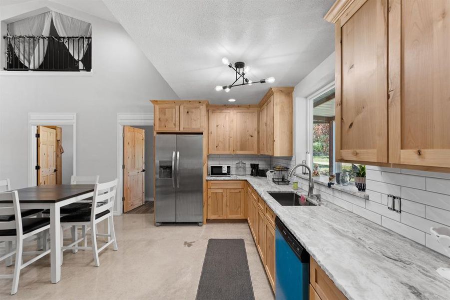 Eat-in-kitchen with knotty alder cabinetry for storage, refrigerator, new dishwasher, disposal, sealed concrete flooring and decorative lighting.