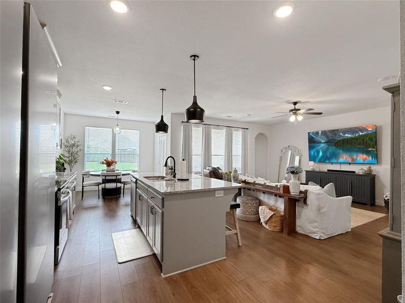 Kitchen featuring appliances with stainless steel finishes, light stone countertops, decorative light fixtures, dark wood-style flooring, and a kitchen island with sink Kitchen featuring appliances with stainless steel finishes, light stone countertops, decorative light fixtures, dark wood-style flooring, and a kitchen island with sink