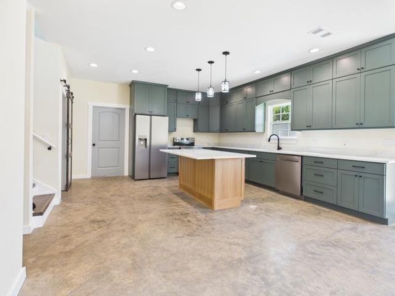 Before Photo featuring concrete floors, stainless steel appliances, pendant lighting, a barn door, and green cabinets