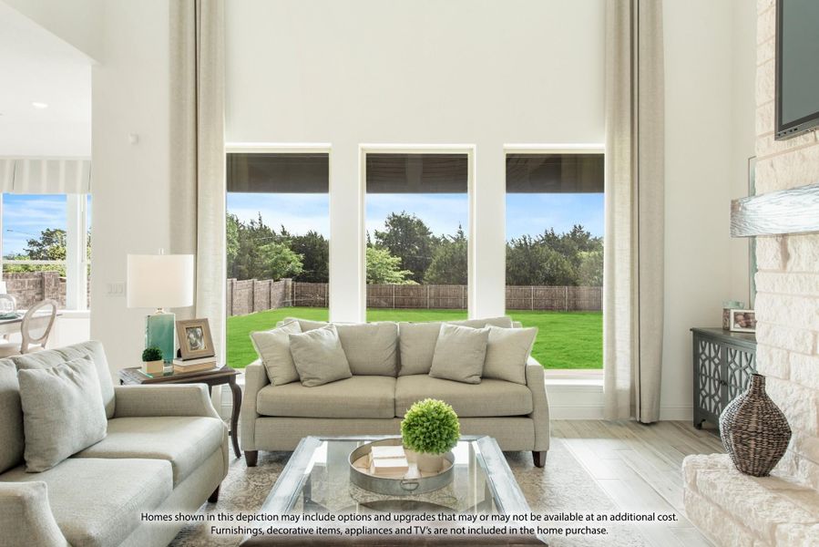 Bright living room with two-story ceilings, large windows, stone fireplace, and neutral sofas overlooking a backyard