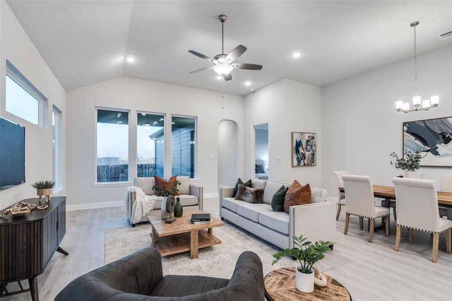 Living room with vaulted ceiling, ceiling fan with notable chandelier, and light wood-type flooring