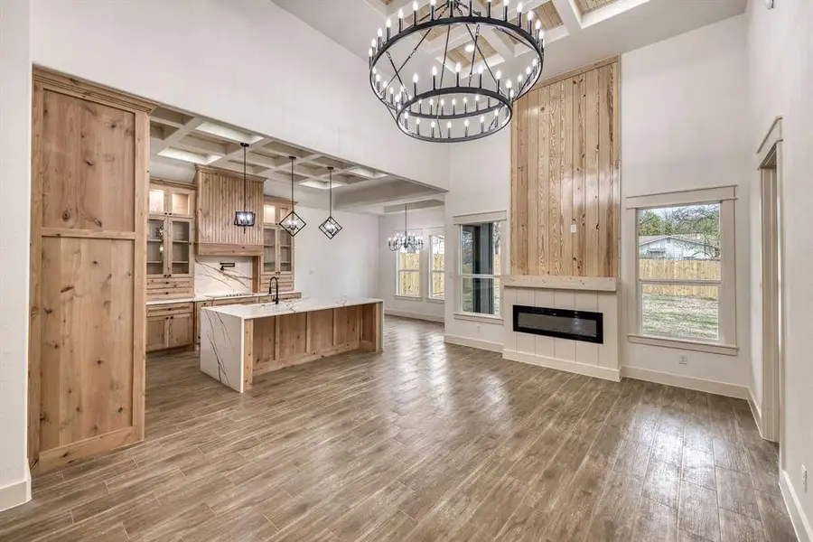 Kitchen featuring a chandelier, coffered ceiling, open floor plan, a large island with sink, and glass fronted cabinets
