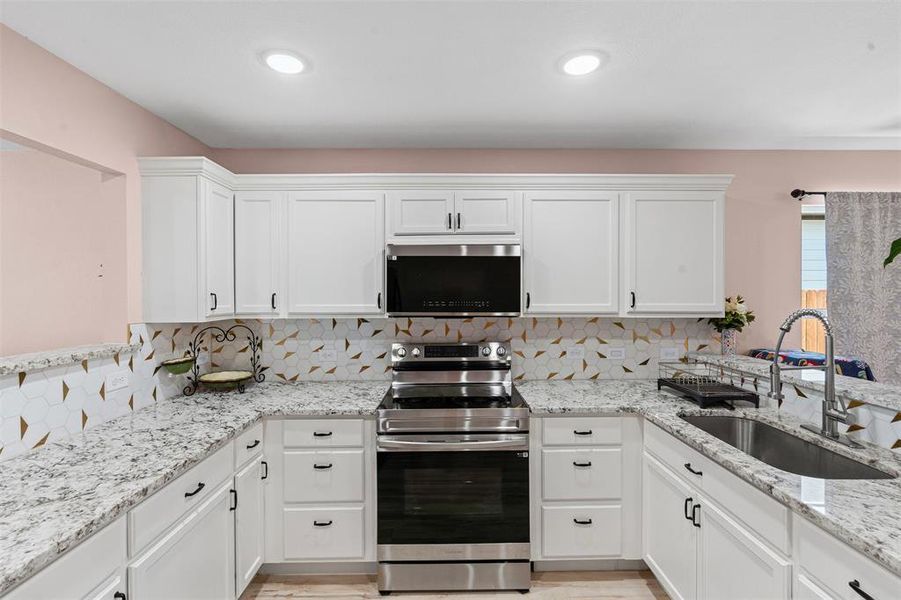 Kitchen featuring stainless steel appliances, white cabinets, light stone counters, decorative backsplash, and a peninsula Kitchen featuring stainless steel appliances, white cabinets, light stone counters, decorative backsplash, and a peninsula