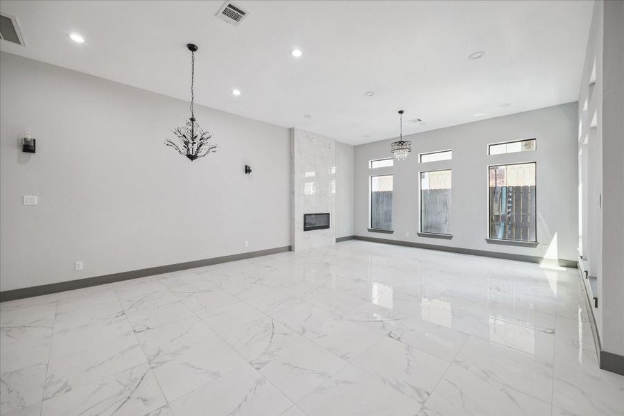 Living room is designed with a sense of openness and elegance, highlighted by its glossy marble-look tile floors that reflect natural light throughout the space. A sleek modern fireplace framed with floor-to-ceiling tile serves as the focal point, adding both style and warmth.