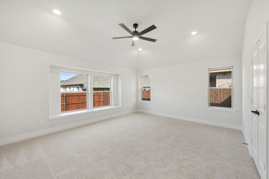 Spacious bedroom with beige carpet, ceiling fan, recessed lighting, and three windows with backyard views.