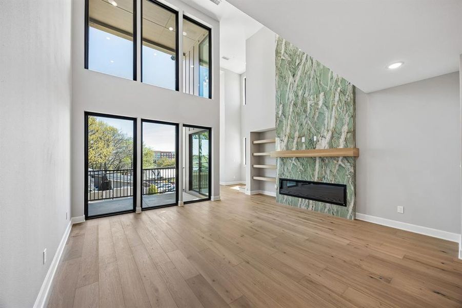 Unfurnished living room with an accent wall, light wood-type flooring, recessed lighting, a large fireplace, and built in features Unfurnished living room with an accent wall, light wood-type flooring, recessed lighting, a large fireplace, and built in features