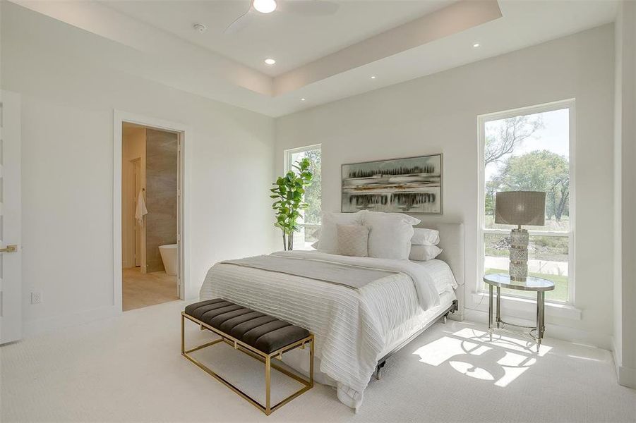 Carpeted bedroom featuring multiple windows, ceiling fan, and ensuite bathroom