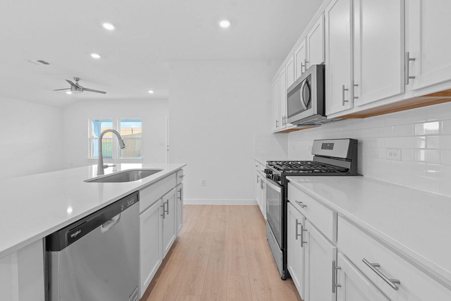 Kitchen with stainless steel appliances, white cabinetry, recessed lighting, light wood-type flooring, and light stone counters
