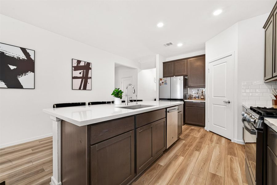 Open-concept kitchen and living area featuring a large quartz island with seating, rich cabinetry, stainless steel appliances, subway tile backsplash, and seamless flow into the main living space. The thoughtfully designed layout is ideal for entertaining while offering a warm, modern aesthetic with abundant natural light throughout.