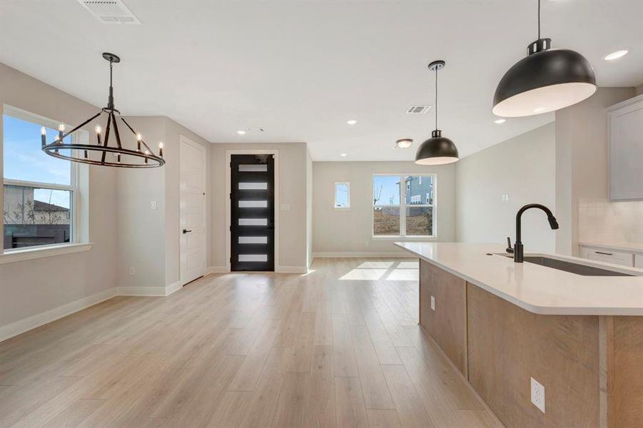 Kitchen featuring open floor plan, light wood-style floors, suspended lighting, an island with sink, and light stone countertops