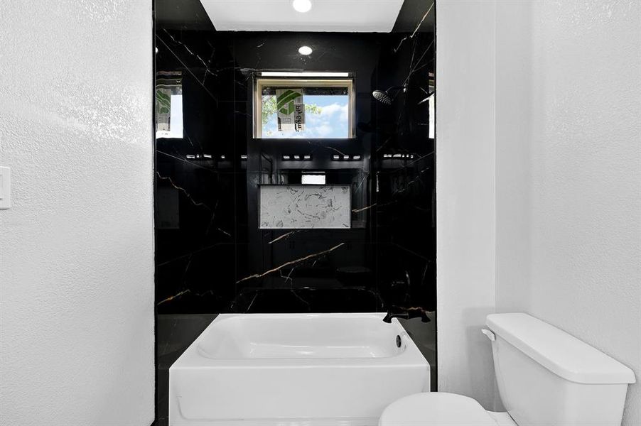 This bathroom features a bath and shower combo, a niche for your essentials, and beautiful floor-to-ceiling tile work.