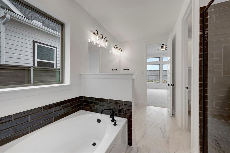 The bathroom features a built-in bathtub with dark tile surround, a large window, and a vanity with dual mirrors and sconce lighting