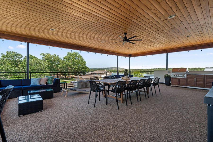 This photo showcases a spacious outdoor patio with a wooden ceiling, ceiling fan, and ample seating. It offers scenic views of waterfront greenery, ideal for entertaining and relaxation.