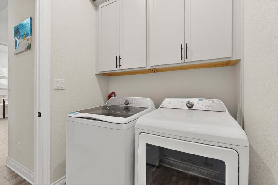 Laundry area with cabinet space, a textured wall, independent washer and dryer, and wood finished floors