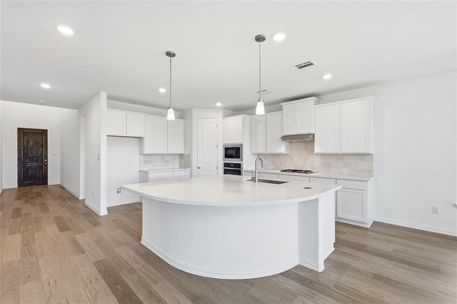 Kitchen featuring white cabinetry, light wood finished floors, a center island with sink, and tasteful backsplash