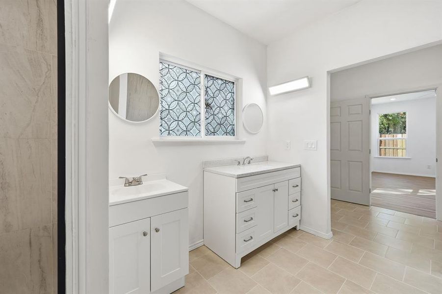 Primary ensuite bathroom with dual vanities, separate tub and shower and light tile patterned floors
