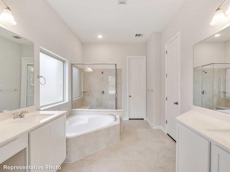Bathroom featuring dual vanities, a spacious corner bathtub, a glass-enclosed shower, and tiled flooring