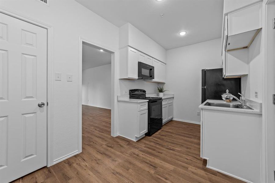 Kitchen with black appliances, dark hardwood / wood-style flooring, sink, and white cabinets