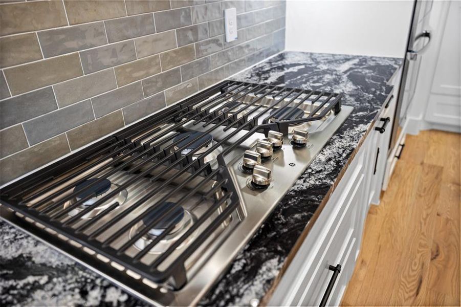 Details featuring hardwood / wood-style floors, decorative backsplash, white cabinetry, and stainless steel gas cooktop