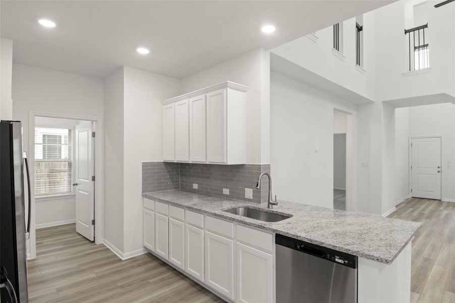 Kitchen featuring dishwasher, freestanding refrigerator, white cabinets, light wood-style floors, and tasteful backsplash Kitchen featuring dishwasher, freestanding refrigerator, white cabinets, light wood-style floors, and tasteful backsplash