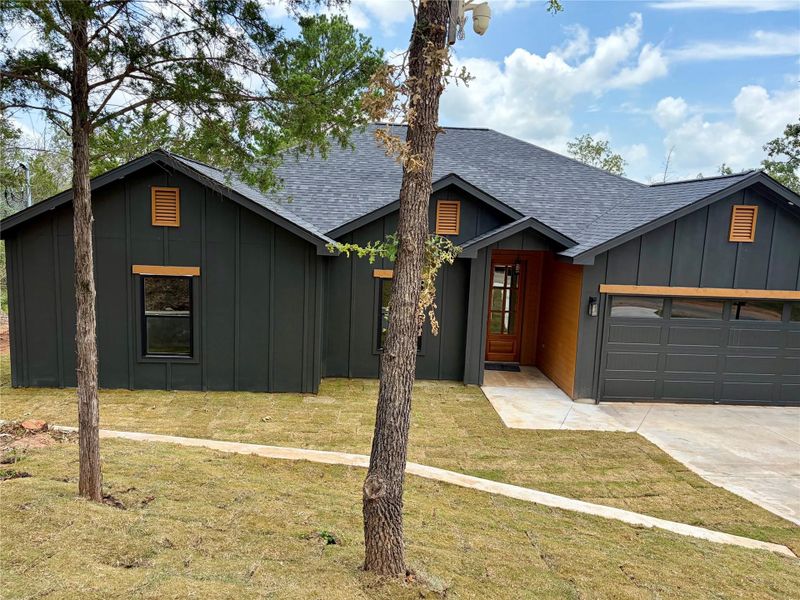 A newly constructed residence showcasing a sophisticated dark vertical siding, wood accents, and a contemporary garage door. A newly constructed residence showcasing a sophisticated dark vertical siding, wood accents, and a contemporary garage door.
