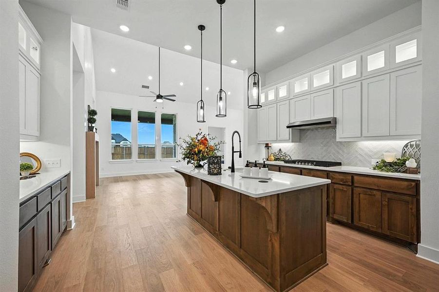 Kitchen featuring glass insert cabinets, hanging light fixtures, backsplash, a kitchen breakfast bar, and an island with sink