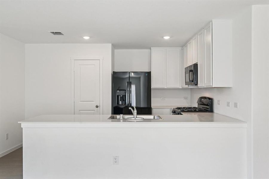 Kitchen featuring black appliances, a peninsula, recessed lighting, white cabinets, and light countertops Kitchen featuring black appliances, a peninsula, recessed lighting, white cabinets, and light countertops