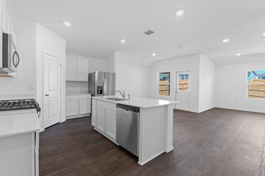 Kitchen featuring stainless steel appliances, dark wood-style flooring, a sink, white cabinetry, and an island with sink