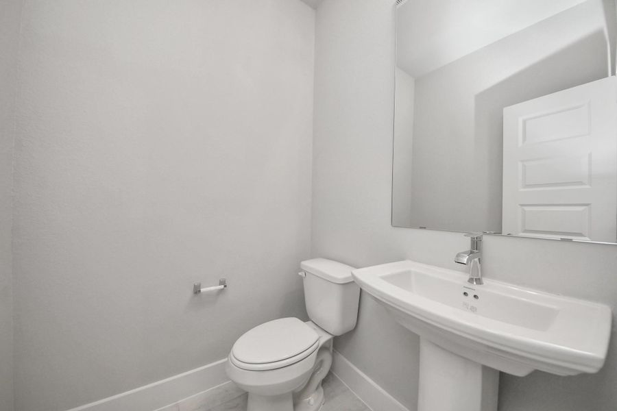 This half bathroom features a stylish pedestal sink, modern hardware, and bright recessed lighting, creating a sleek and inviting space. Sample photo of completed home with similar floor plan. Actual colors and selections may vary.