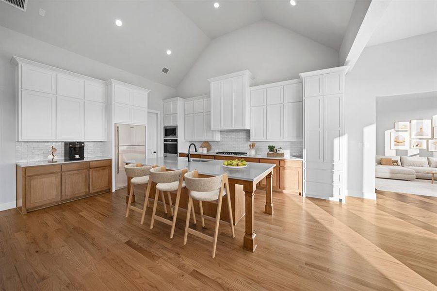 Kitchen featuring tasteful backsplash, white cabinets, high vaulted ceiling, a kitchen bar, and light wood-style flooring Kitchen featuring tasteful backsplash, white cabinets, high vaulted ceiling, a kitchen bar, and light wood-style flooring