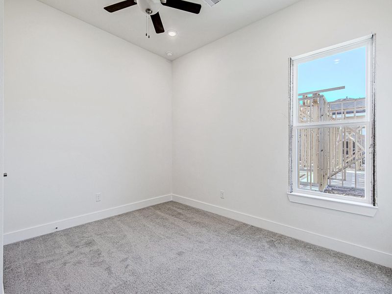 Secondary bedroom with carpet flooring, ceiling fan, and window.