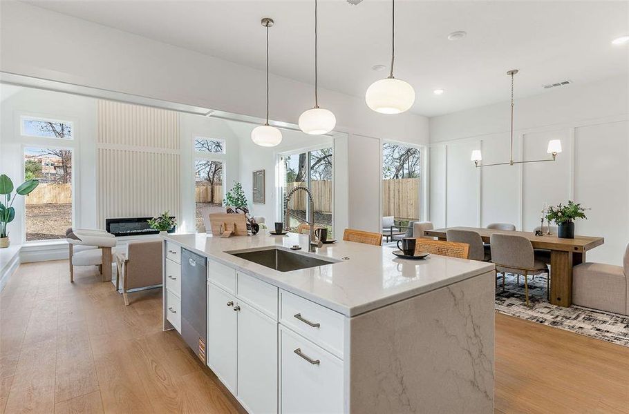 Kitchen with hanging light fixtures, light stone countertops, white cabinets, and light wood-style flooring
