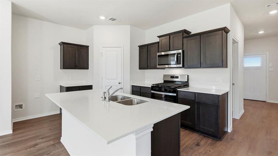 Kitchen with appliances with stainless steel finishes, light stone counters, a center island with sink, recessed lighting, and dark wood-style floors Kitchen with appliances with stainless steel finishes, light stone counters, a center island with sink, recessed lighting, and dark wood-style floors