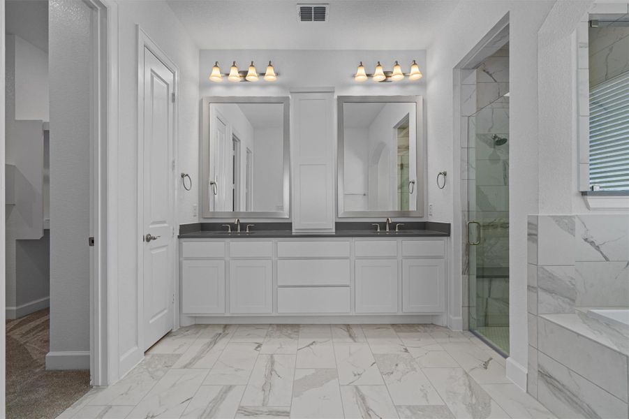 Spacious bathroom featuring dual white vanities with dark countertops, two framed mirrors, and overhead vanity lighting