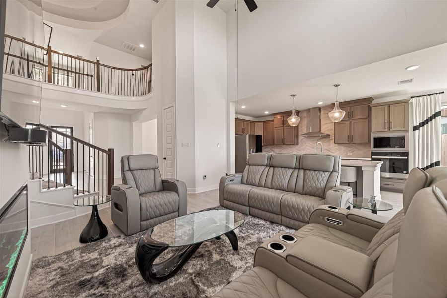 This photo showcases a modern, open-concept living space with high ceilings and elegant design. It features a spacious seating area with plush leather sofas, a stylish glass coffee table, and a contemporary kitchen with stainless steel appliances and pendant lighting. The room is bright and inviting, perfect for entertaining.