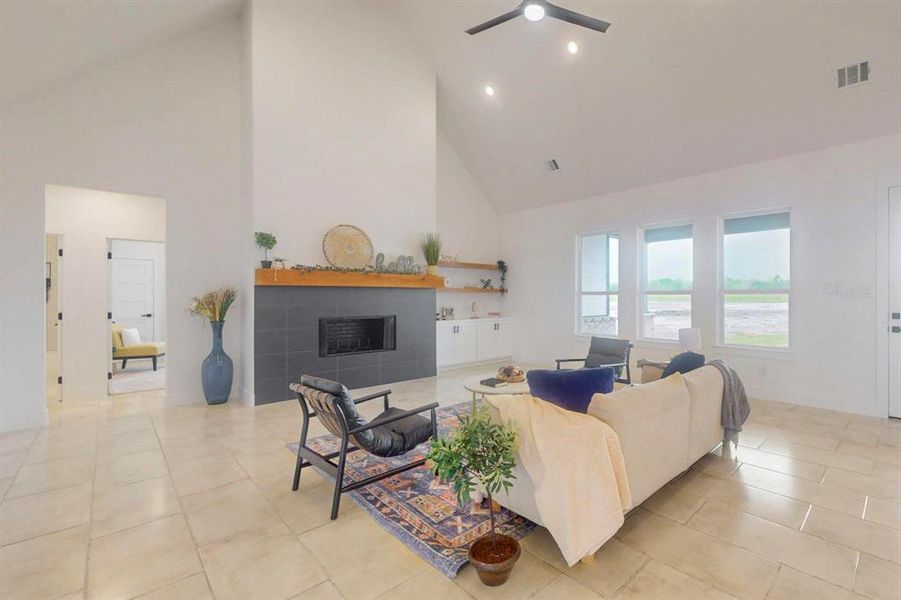 Living room with light tile patterned flooring, high vaulted ceiling, a tile fireplace, visible vents, and ceiling fan Living room with light tile patterned flooring, high vaulted ceiling, a tile fireplace, visible vents, and ceiling fan
