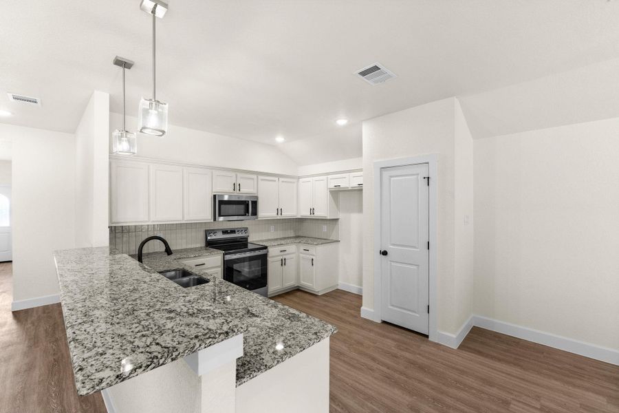 Kitchen with stainless steel appliances, white cabinets, backsplash, decorative light fixtures, and vaulted ceiling