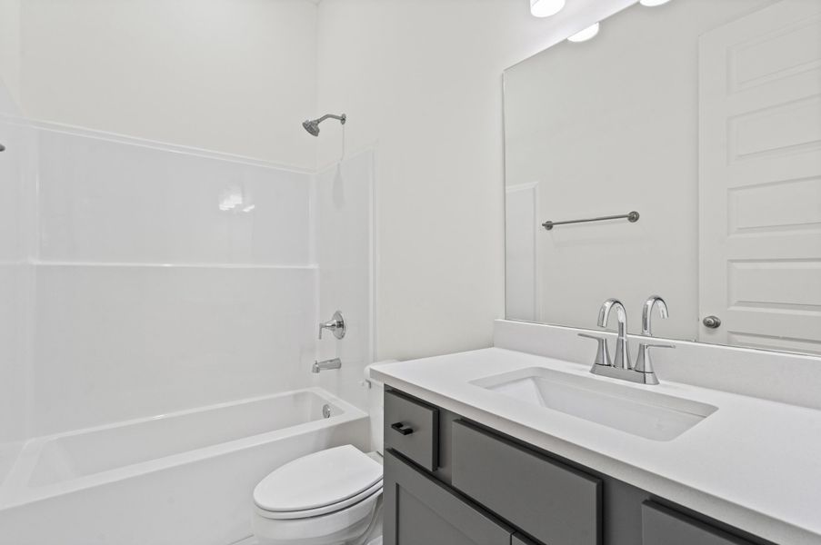 Bathroom featuring a white integrated sink, gray cabinet vanity with black hardware, white tub-shower combination, polished chrome fixtures, and a large wall-mounted mirror
