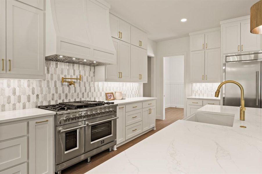 Kitchen featuring premium appliances, tasteful backsplash, custom exhaust hood, white cabinetry, and recessed lighting Kitchen featuring premium appliances, tasteful backsplash, custom exhaust hood, white cabinetry, and recessed lighting