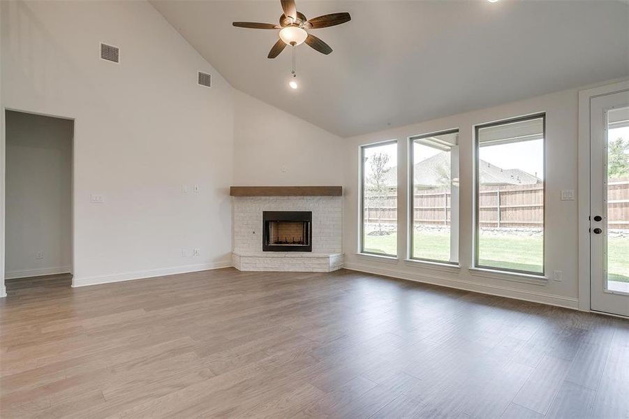 Unfurnished living room with light hardwood / wood-style flooring, ceiling fan, high vaulted ceiling, and a fireplace