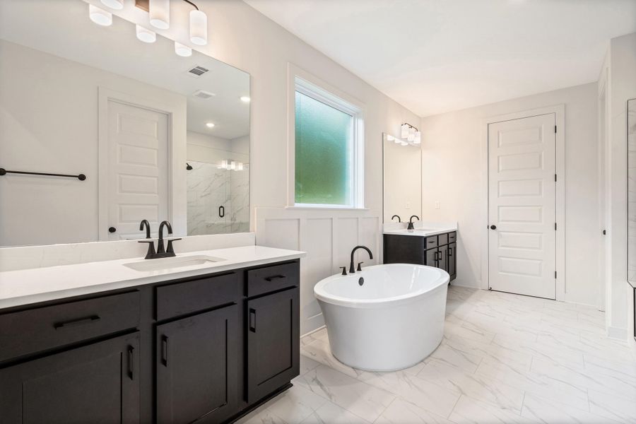 Spacious bathroom featuring a freestanding oval tub with matte black fixtures, dual dark wood-finish vanities with white countertops, a walk-in shower with a glass enclosure, and white tile flooring throughout Spacious bathroom featuring a freestanding oval tub with matte black fixtures, dual dark wood-finish vanities with white countertops, a walk-in shower with a glass enclosure, and white tile flooring throughout